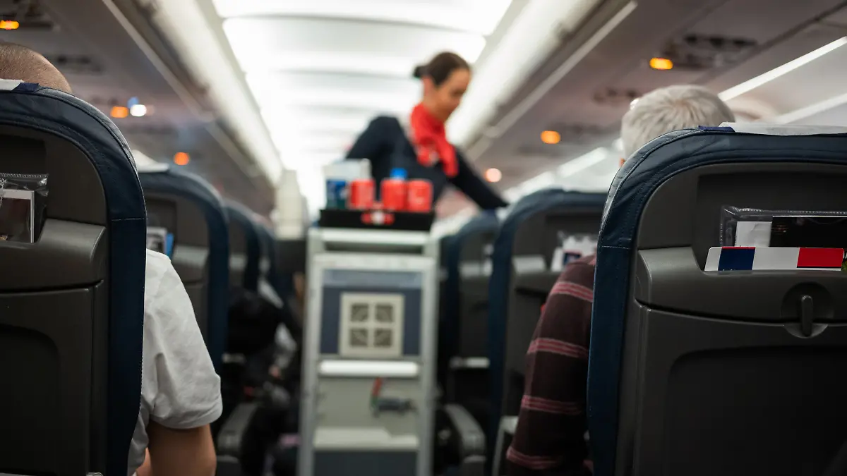 Eine Flugbegleiterin steht im Gang eines Flugzeugs und verteilt Getränke.