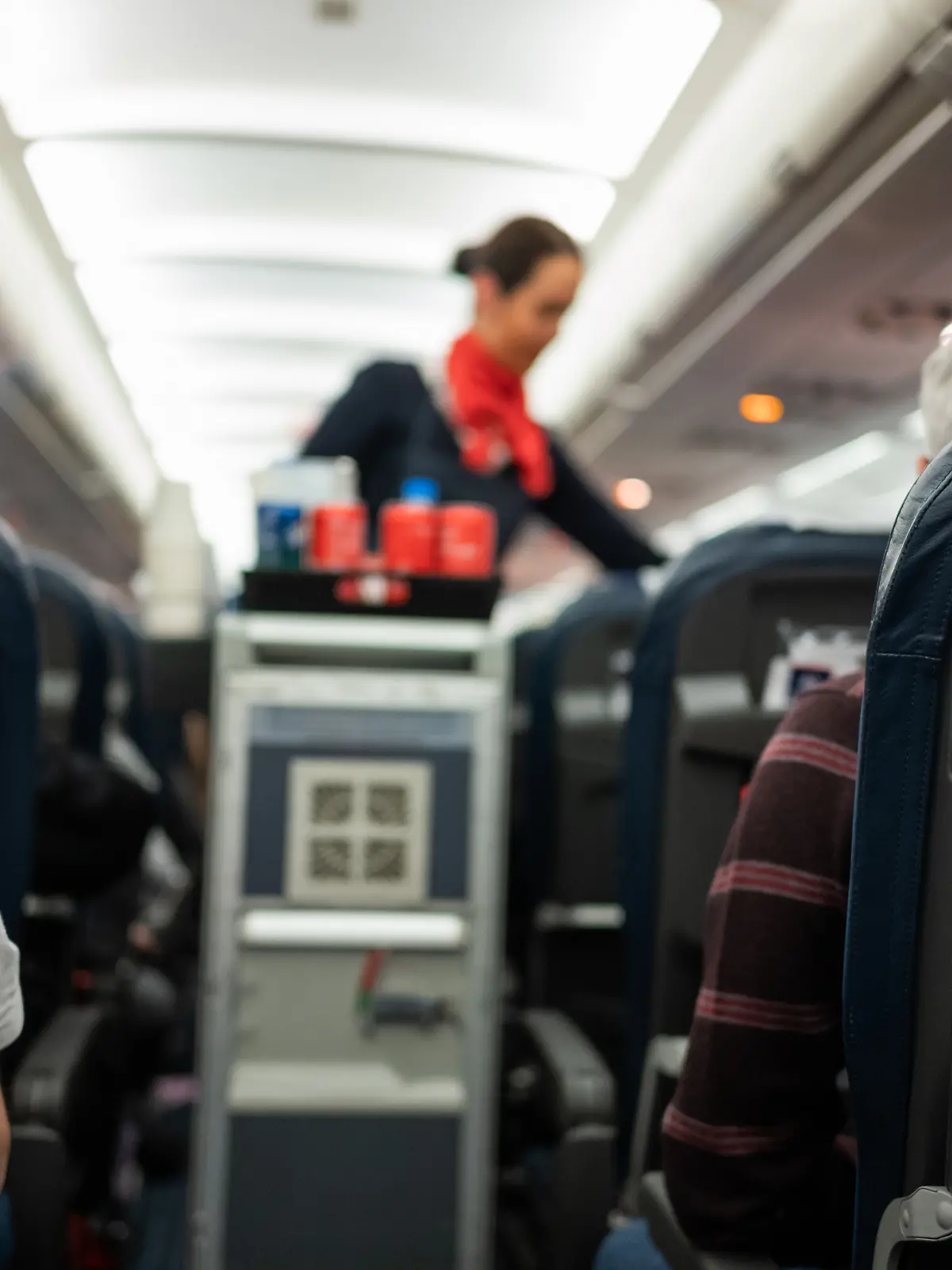 Eine Flugbegleiterin steht im Gang eines Flugzeugs und verteilt Getränke.