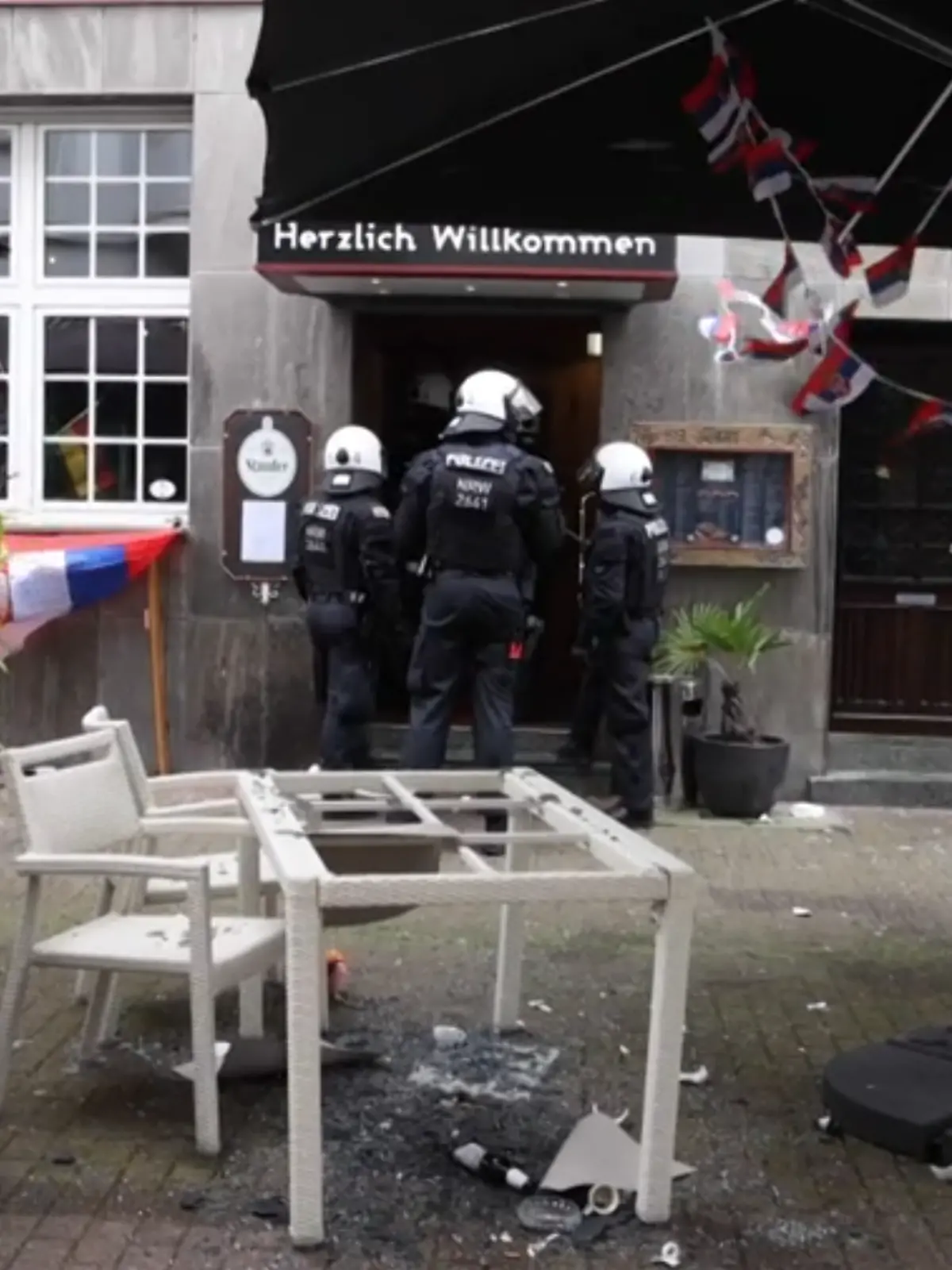 Polizisten stehen vor einem Restaurant, die Terrasse ist verwüstet. 