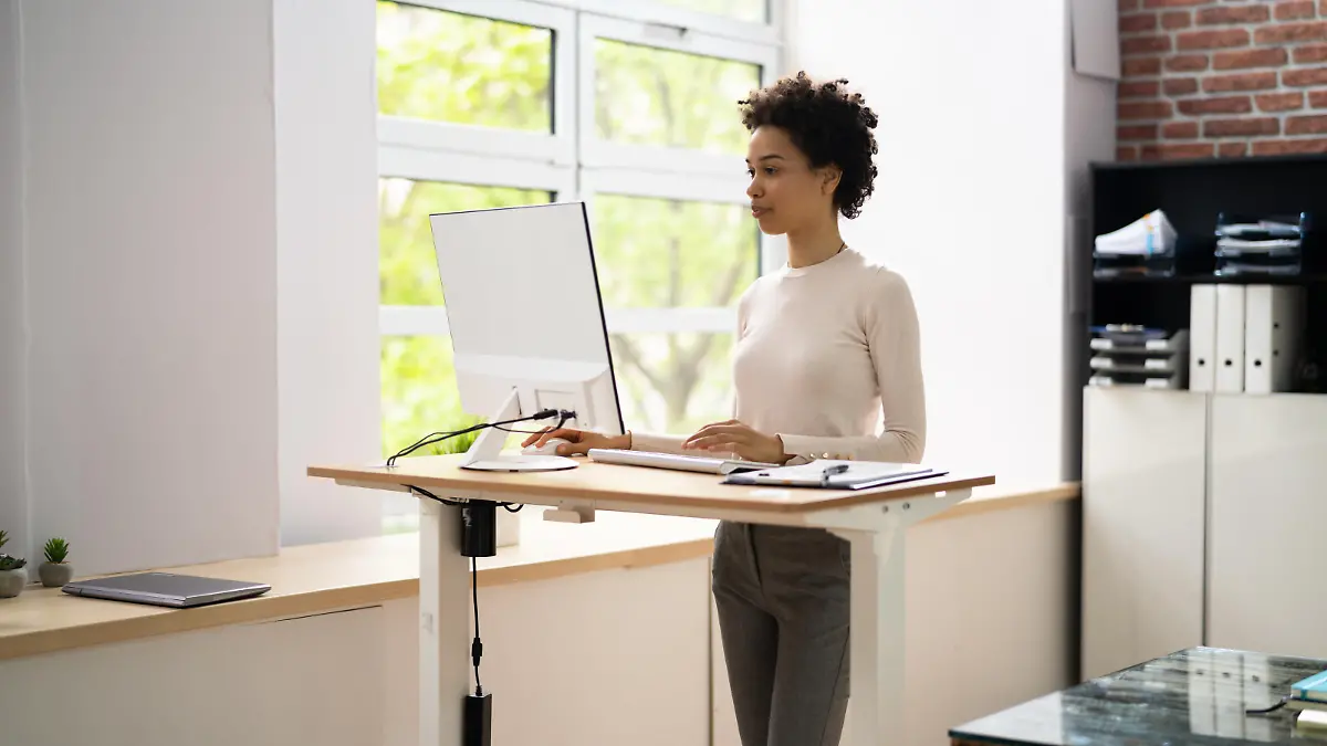 Woman Using Adjustable Height Standing Desk In Office For Good Posture