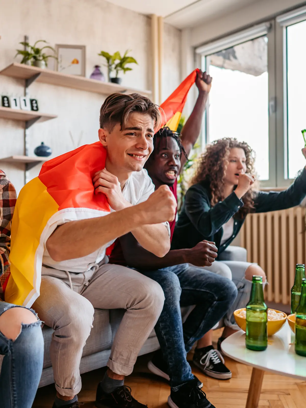 Gruppe Freunde jubelt während des Deutschlandspiels vor dem Fernseher.
