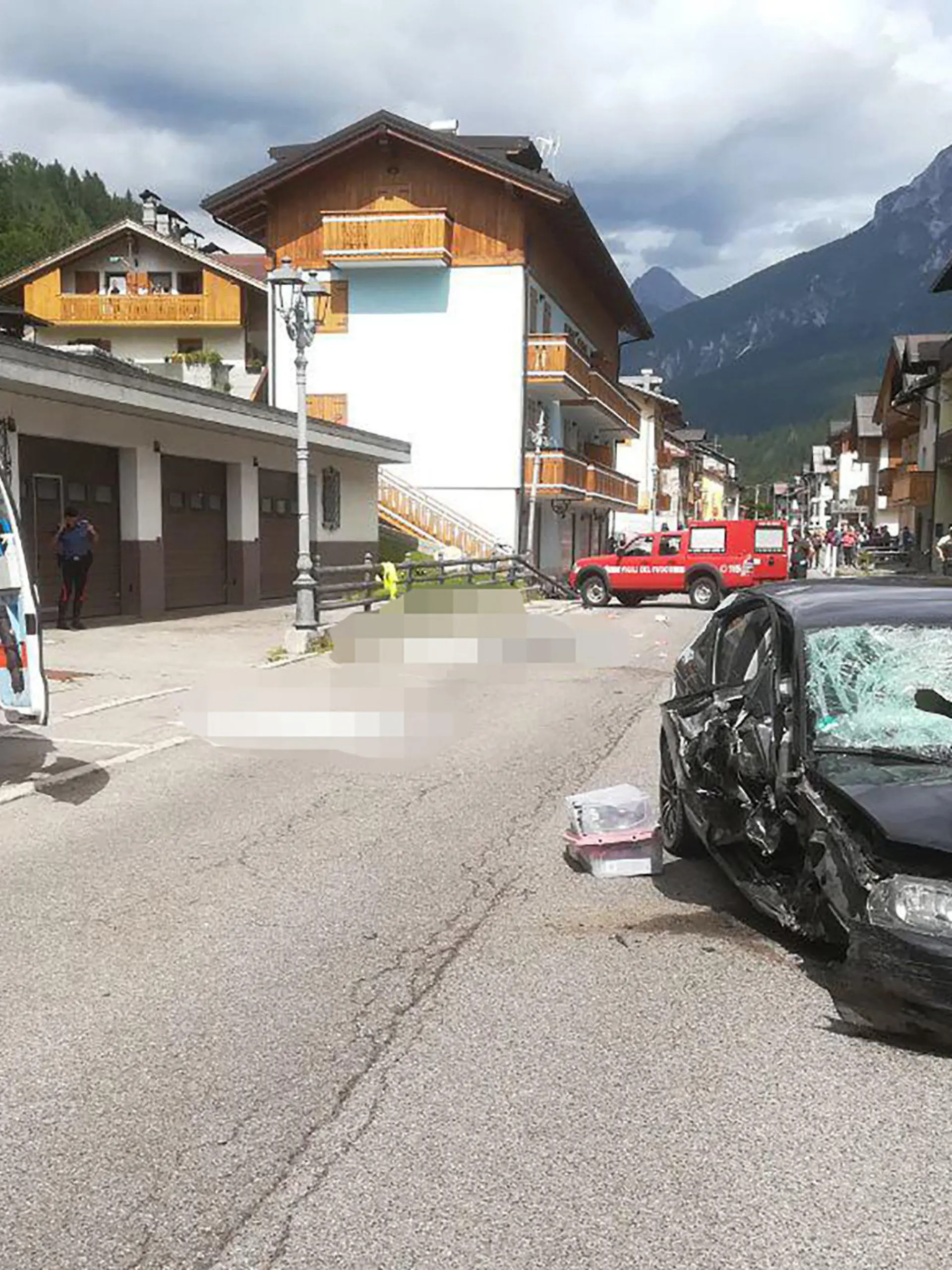 HANDOUT - 07.07.2023, Italien, Santo Stefano di Cadore: Ein Krankenwagen und das Auto der Deutschen stehen nach dem Unfall neben den Opfern (gepixelt), die auf einer Straße liegen. Eine Deutsche soll in Norditalien mit ihrem Auto in eine Familie gerast sein und drei Menschen getötet haben. Die Frau wurde nach dem Unfall am Donnerstag, 06.07.2023 festgenommen. Die Frau soll am Donnerstagnachmittag mit ihrem Auto in der Ortschaft nahe der Grenze zu Österreich mit hoher Geschwindigkeit in die Familie gefahren sein. Die Großmutter, der Vater und ein zwei Jahre alter Junge starben bei der Kollision. Die Mutter wurde leicht verletzt. Der Großvater, der offenbar mit etwas Abstand lief, kam wegen eines Schocks in eine Klinik. Foto: -/Vigili del fuoco/dpa - ACHTUNG: Nur zur redaktionellen Verwendung im Zusammenhang und nur mit vollständiger Nennung des vorstehenden Credits; Opfer des Unfalls wurden aus rechtlichen Gründen gepixelt +++ dpa-Bildfunk +++