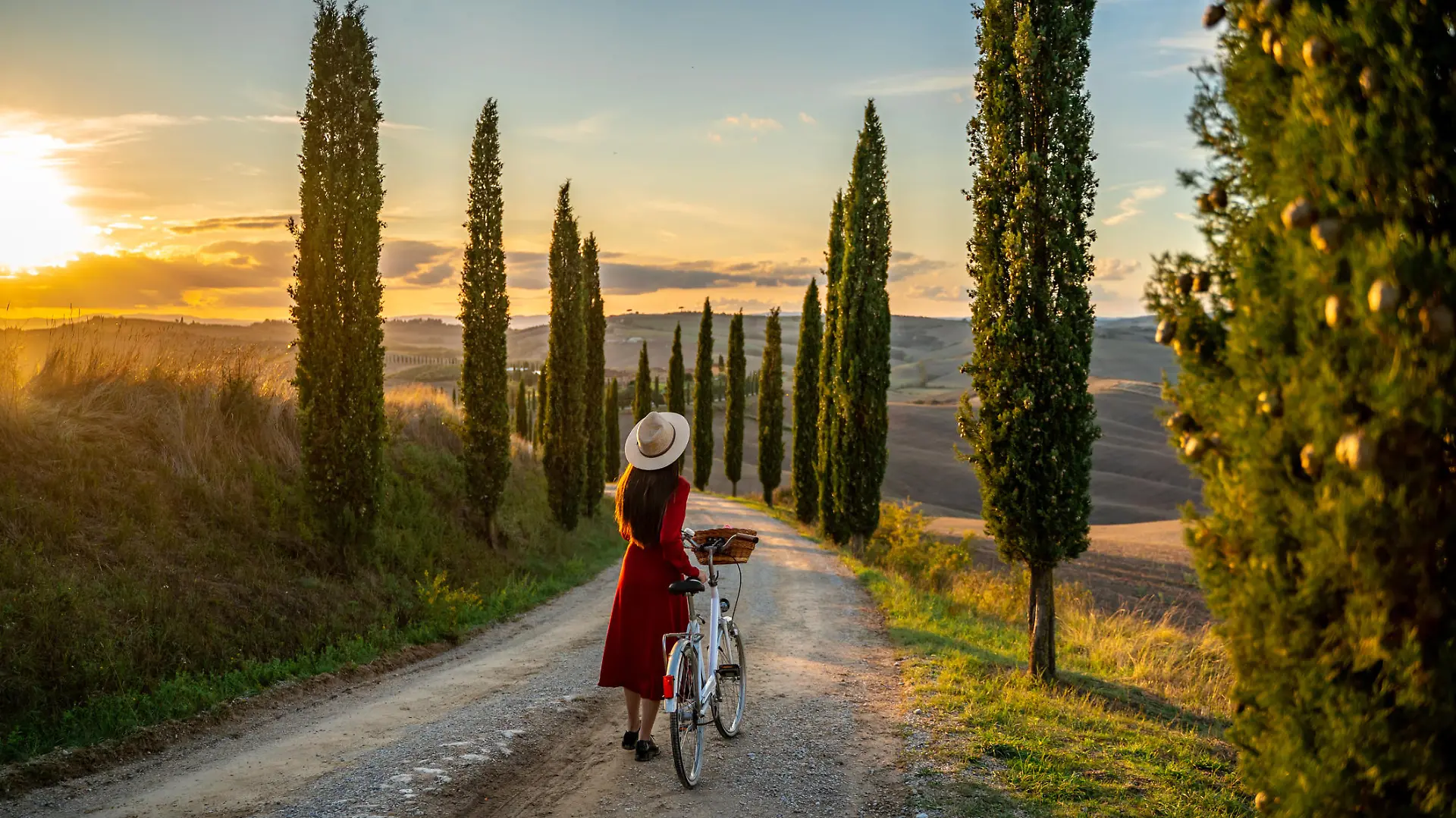 Young girl in red dress watching the sunset sitting on a vintage bicycle