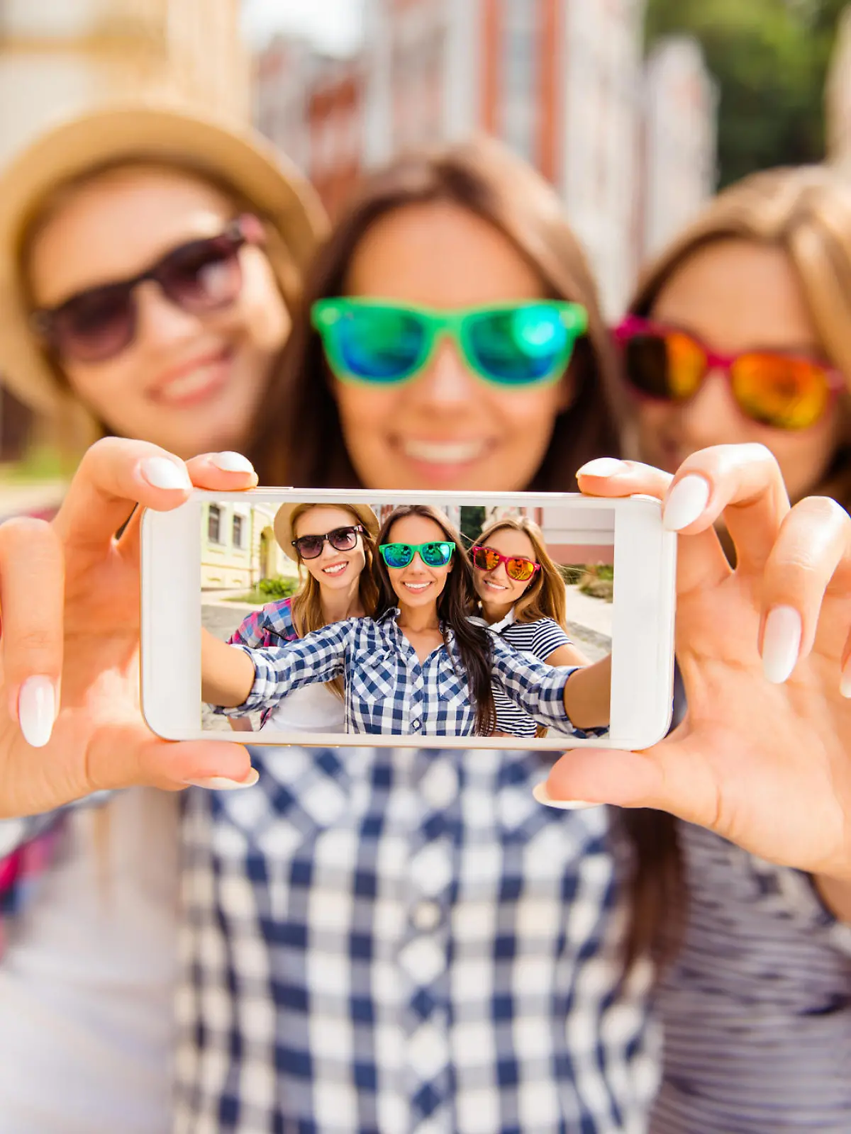 Three happy best girlfriends in glasses making selfie on smartphone