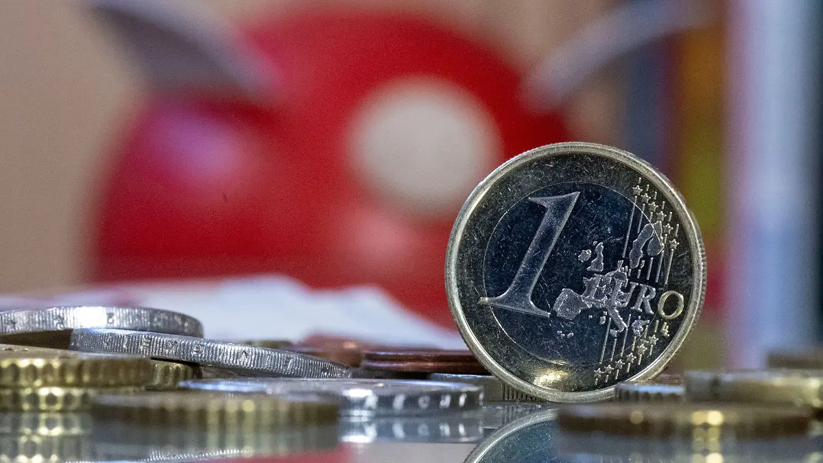 Eine 1 Euro Münze steht auf einem Tisch vor einem Sparschwein. Nach jahrelanger Durststrecke haben Millionen Sparer 2023 erstmals wieder im größeren Stil von gestiegenen Zinsen profitiert.
