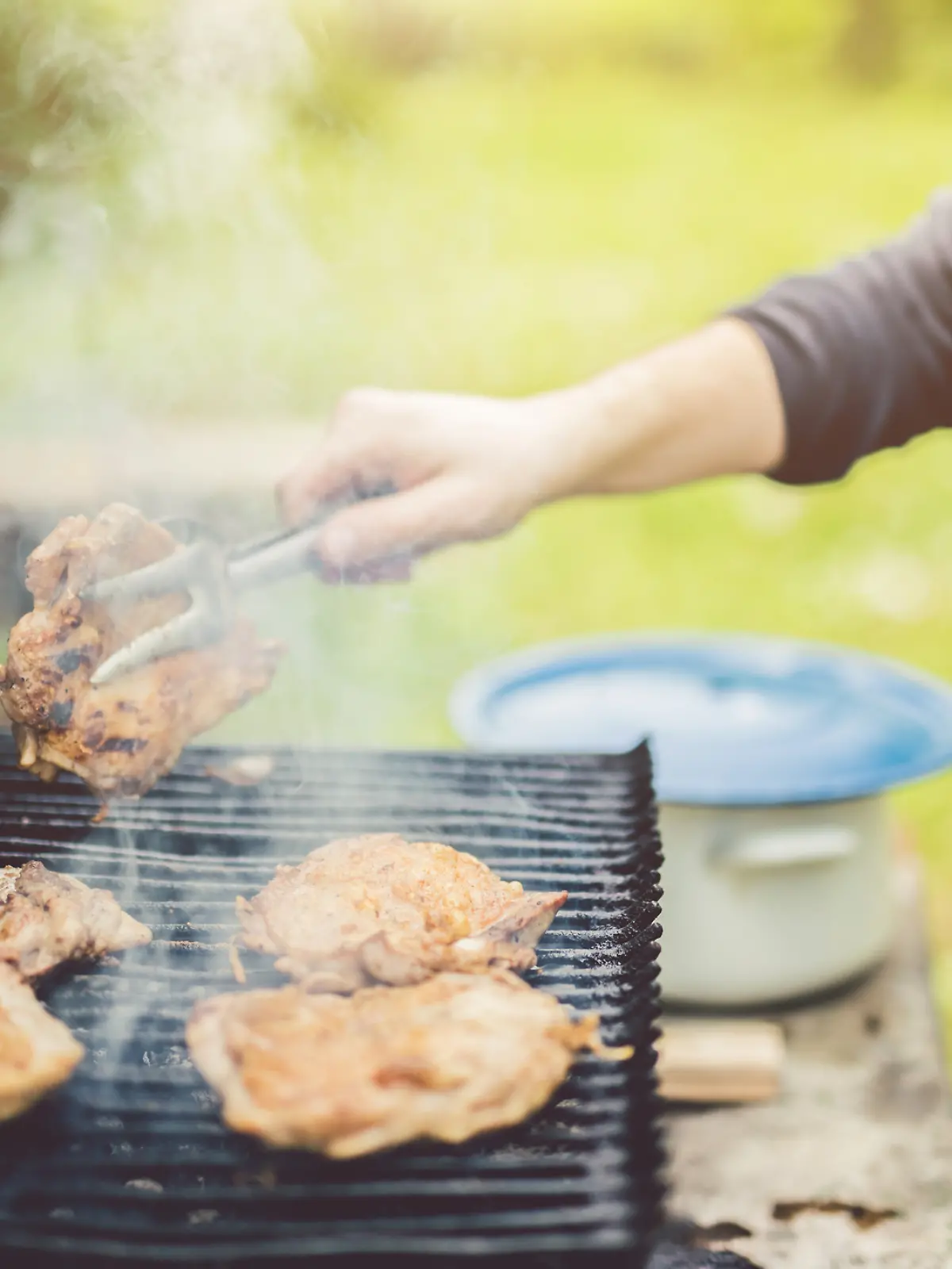 Ein Mann rät Hähnchenfleisch auf einem Grill an.