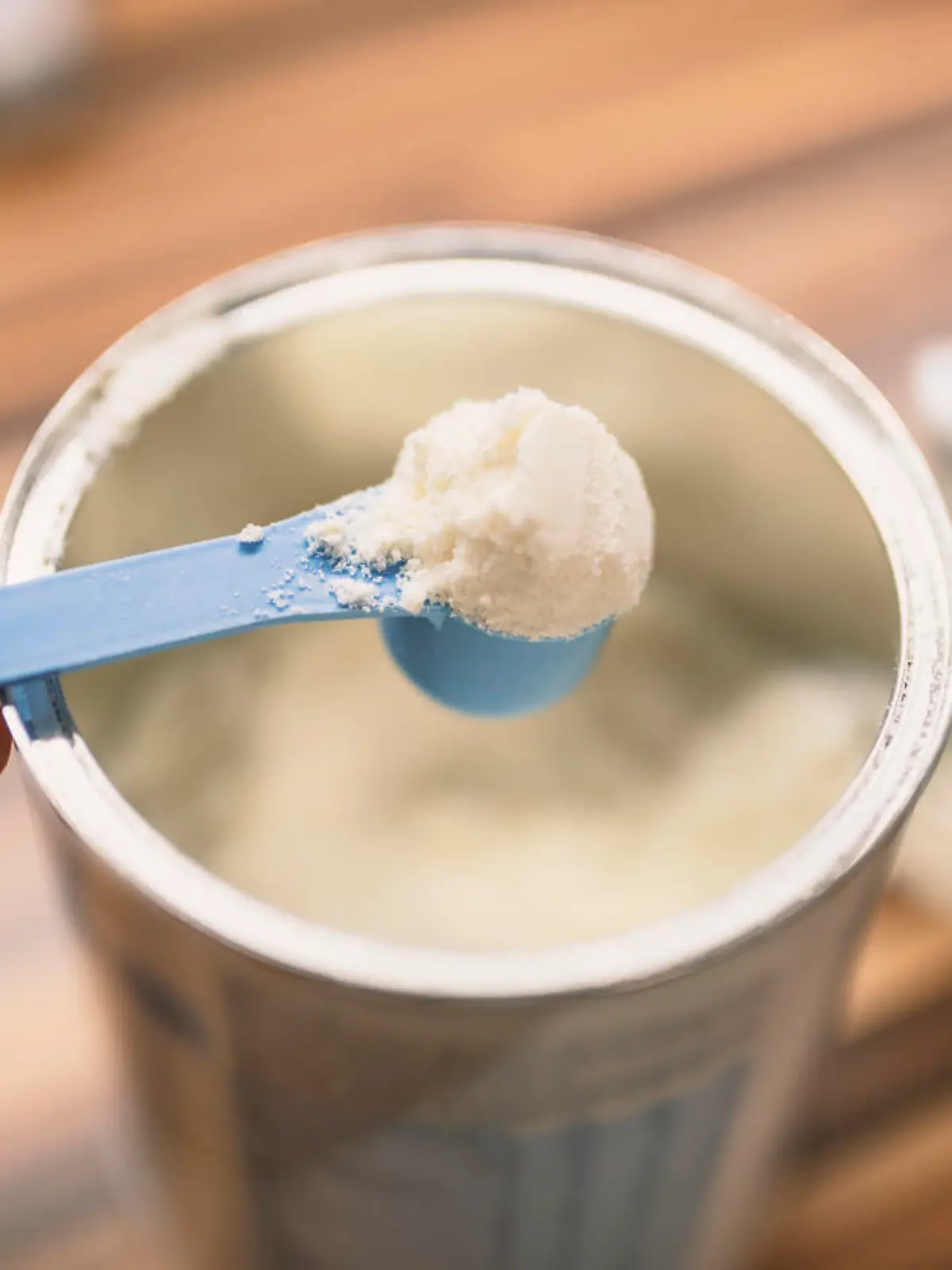 Powder milk for baby and blue spoon on light background close-up. Milk powder for baby in measuring spoon on can. Powdered milk with spoon for baby. Baby Milk Formula and Baby Bottles. Baby milk formula on kitchen background