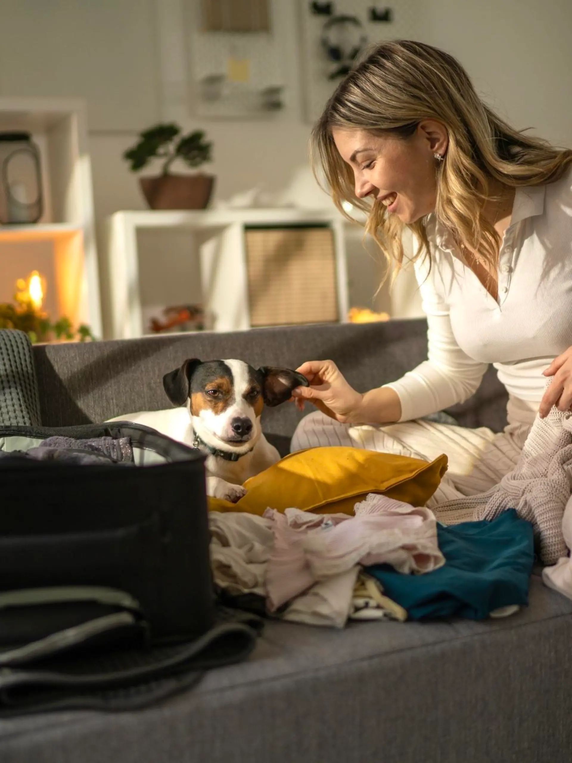Woman packs things in a suitcase, her dog is giving her company
