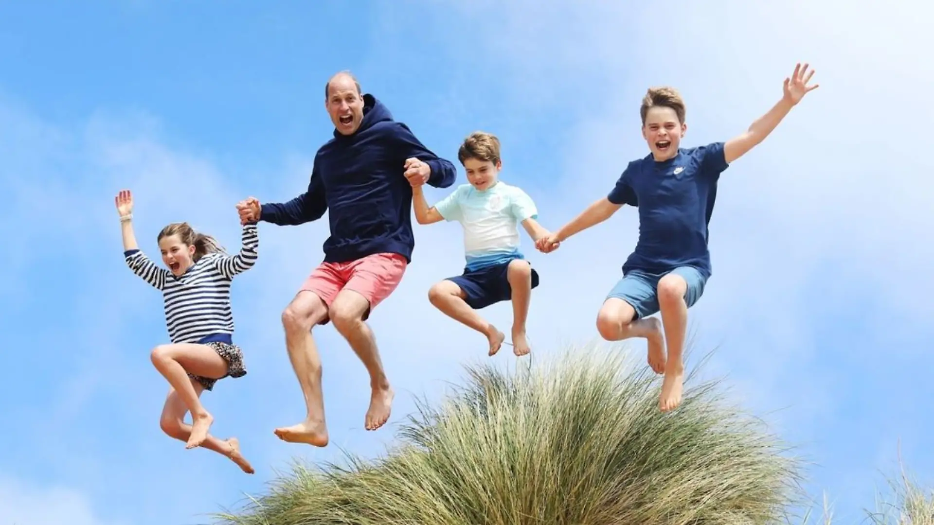Prinz William und die Kinder springen über eine Dühne am Strand