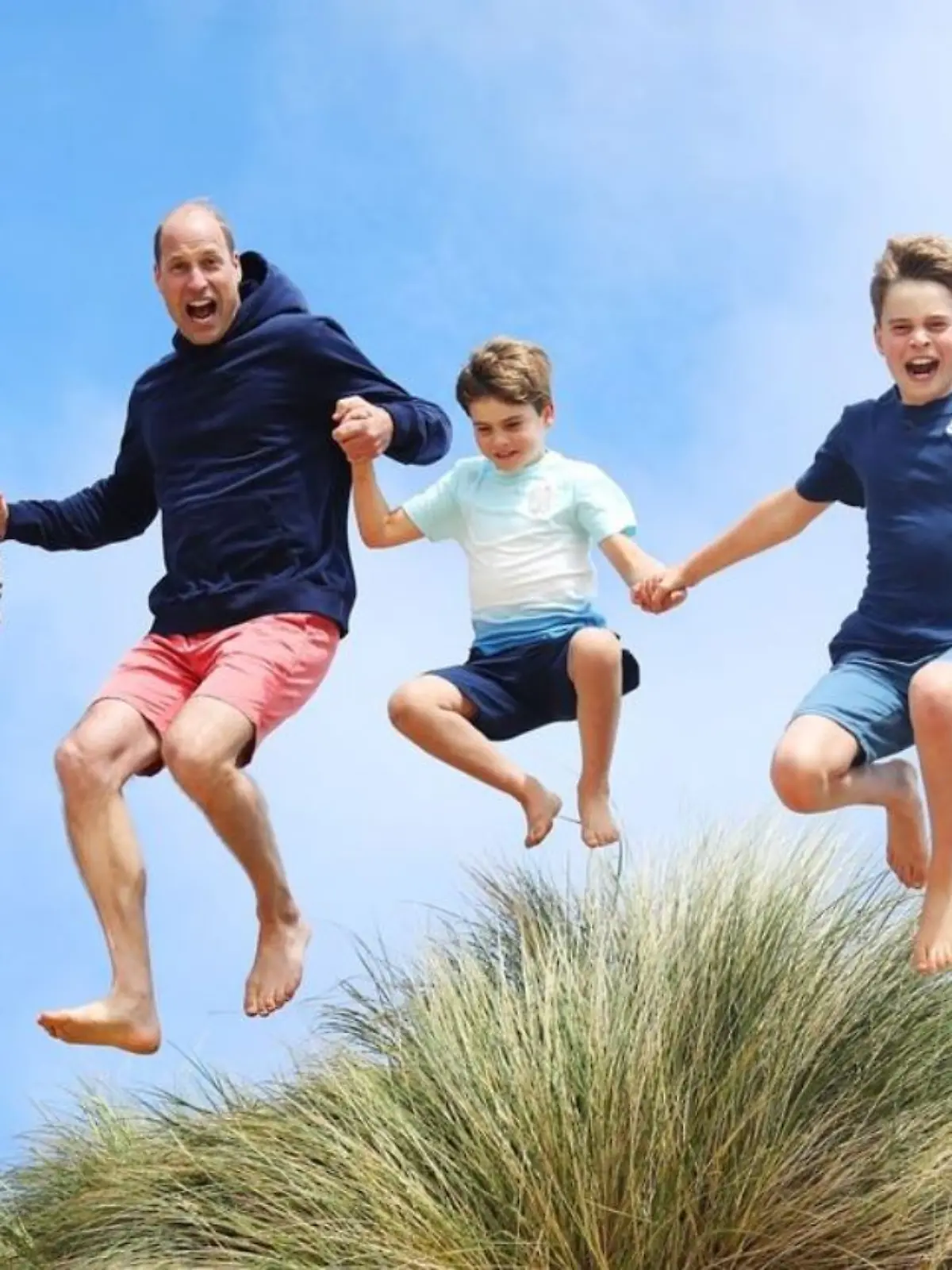 Prinz William und die Kinder springen über eine Dühne am Strand
