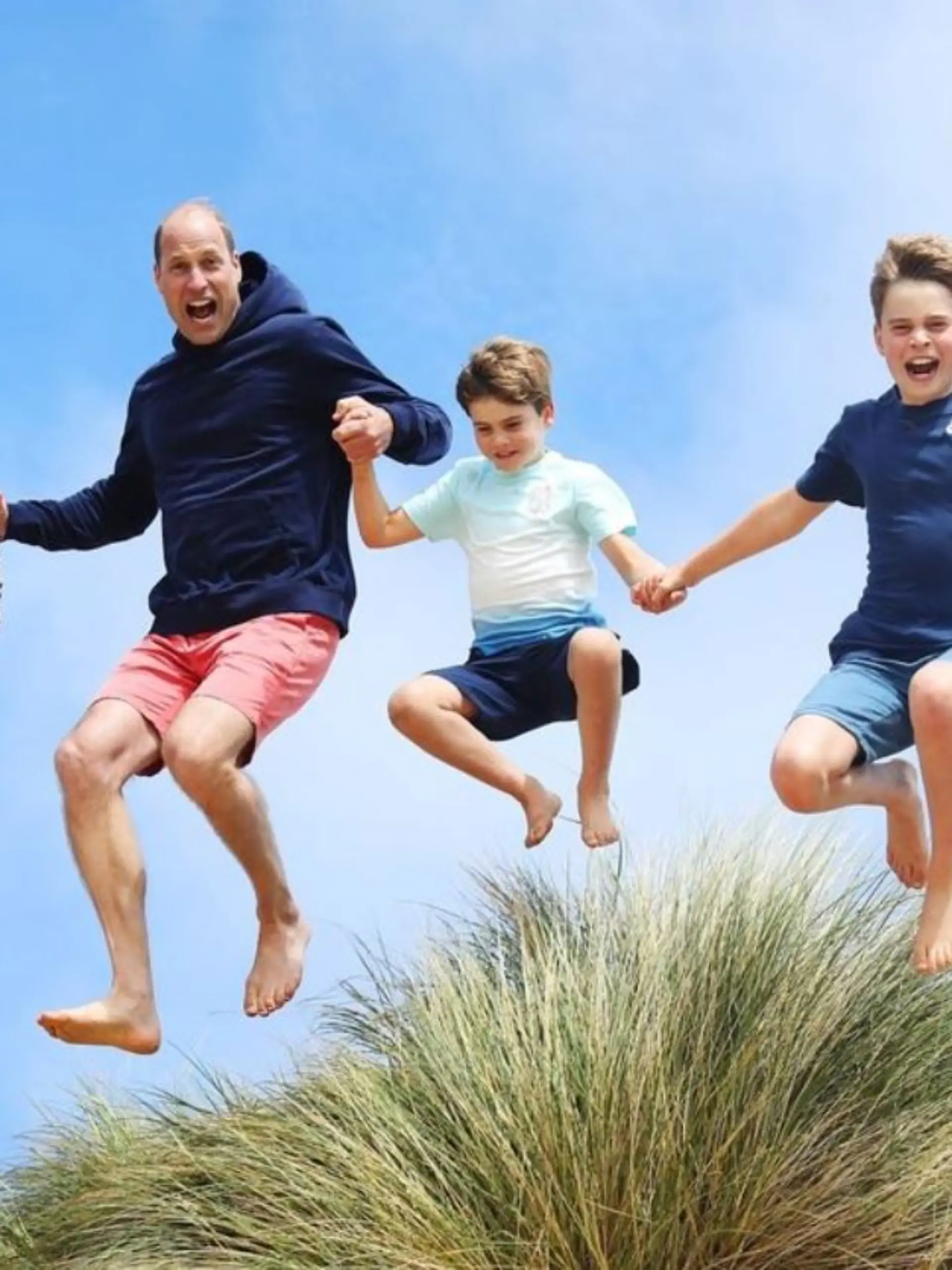 Prinz William und die Kinder springen über eine Dühne am Strand