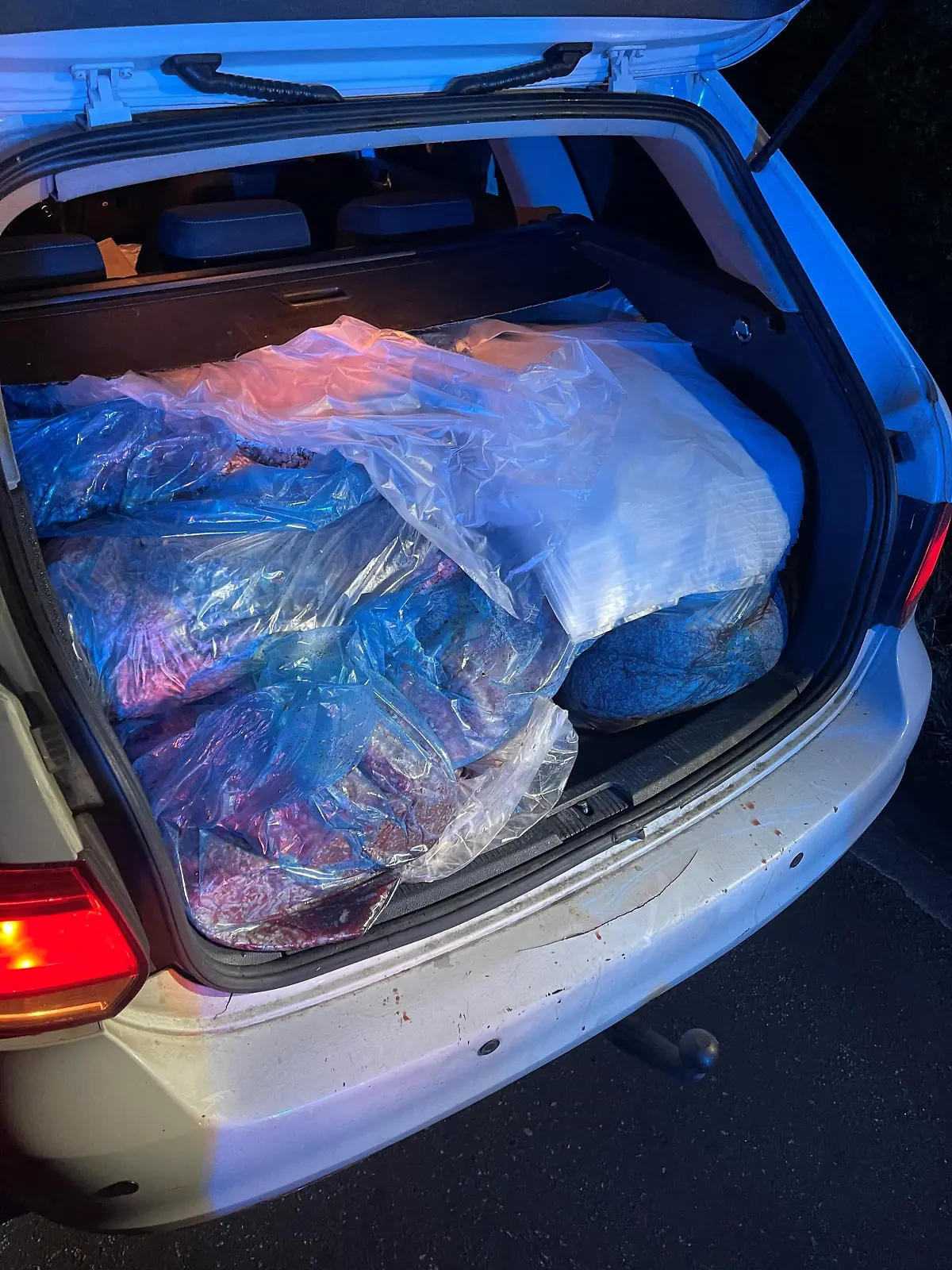 Ein silbernes AUto mit geöffnetem Kofferraum, in dem viele Tüten mit Hackfleisch zu sehen sind.
