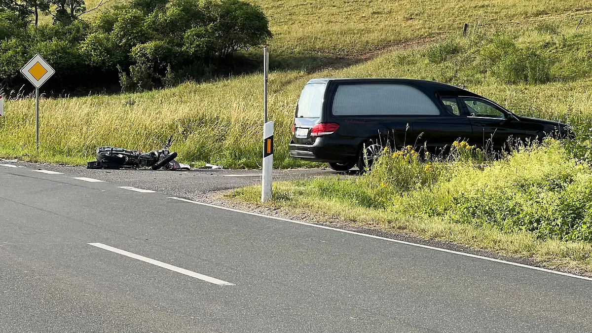 Das Fahrzeug eines Bestatters steht nach einem Unfall neben einem Motorrad, das am Boden liegt.