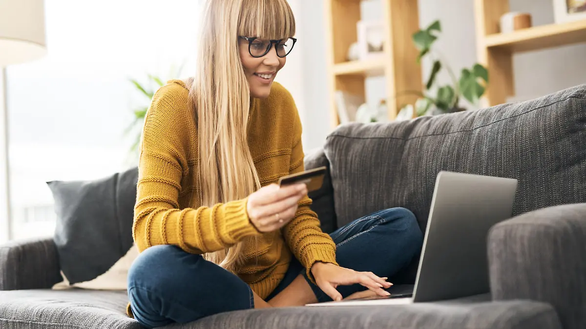Shot of a young woman using a laptop and credit card on the sofa at home