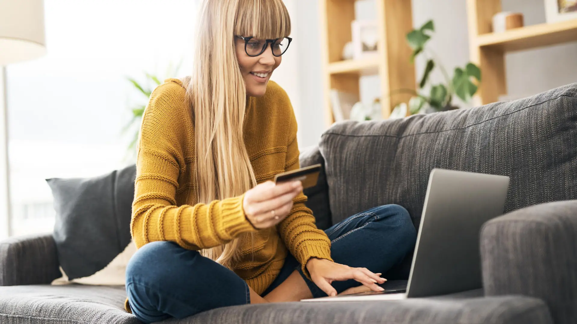 Shot of a young woman using a laptop and credit card on the sofa at home