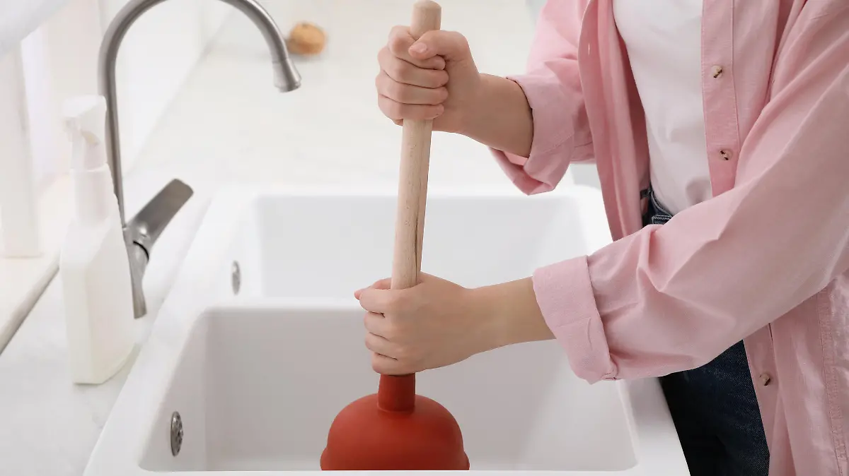 Woman using plunger to unclog sink drain in kitchen, closeup