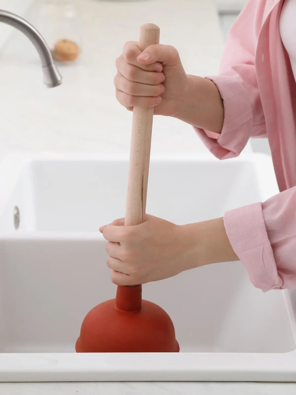 Woman using plunger to unclog sink drain in kitchen, closeup