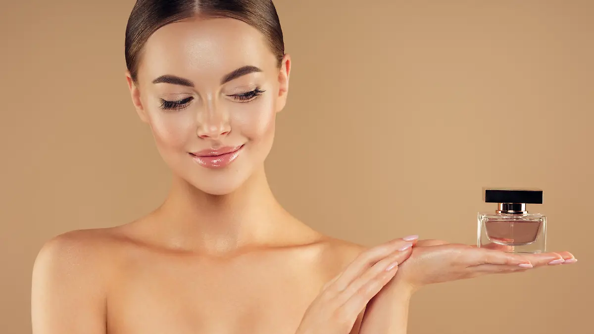 Young woman with clean and fresh skin presenting perfume
