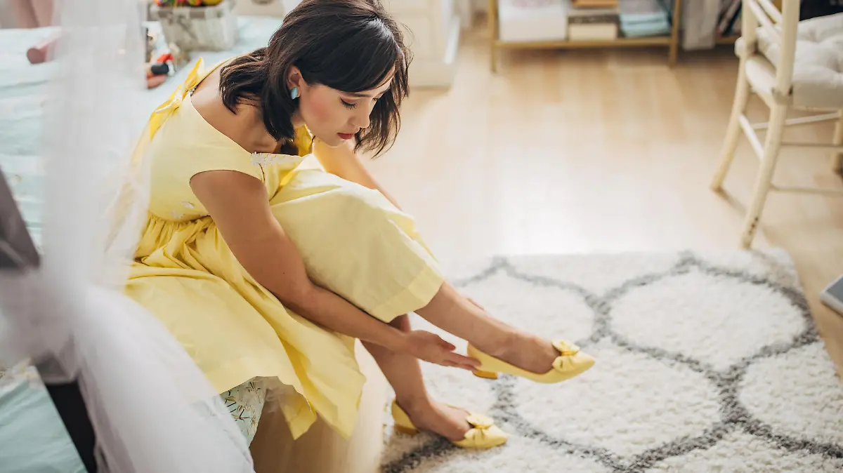 Classy young woman choosing and trying on shoes in her bedroom at home.