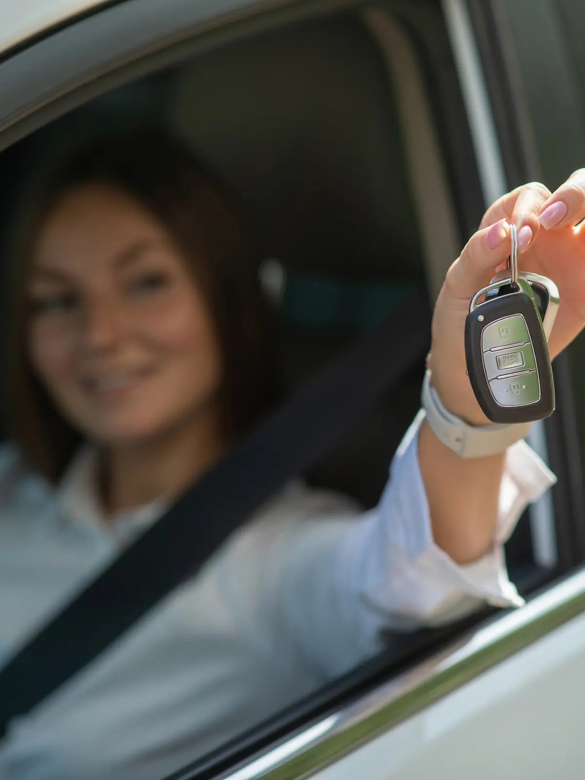 Frau sitzt im Auto und hält ihren Autoschlüssel durchs Fenster.