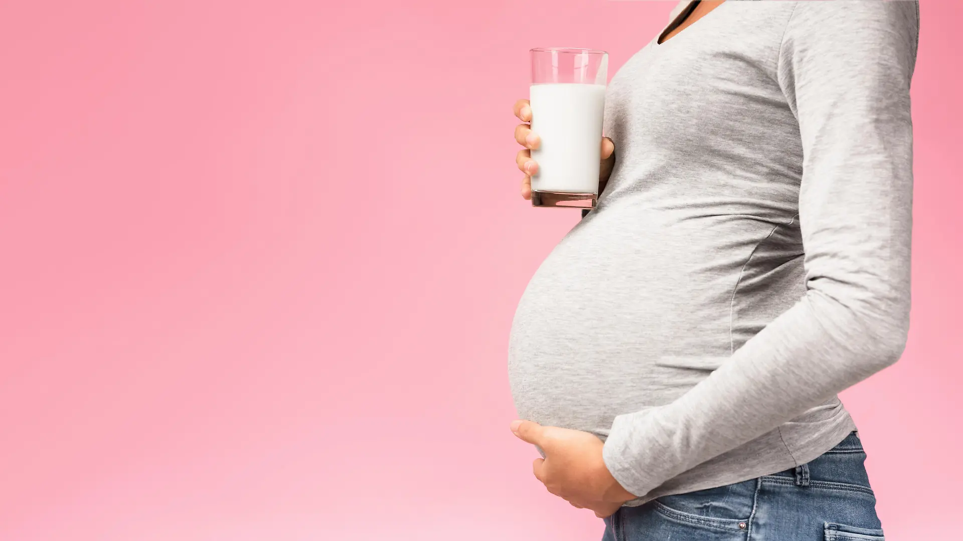 Healthy nutrition. Unrecognizable pregnant woman with glass of milk, pink background, panorama with free space