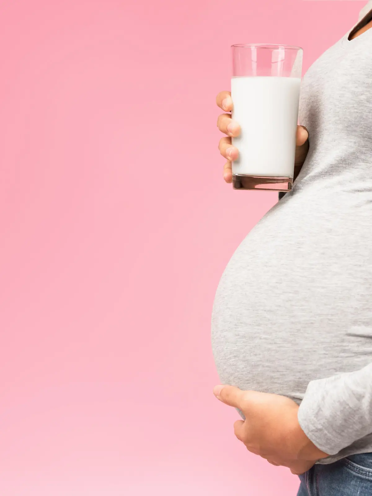 Healthy nutrition. Unrecognizable pregnant woman with glass of milk, pink background, panorama with free space