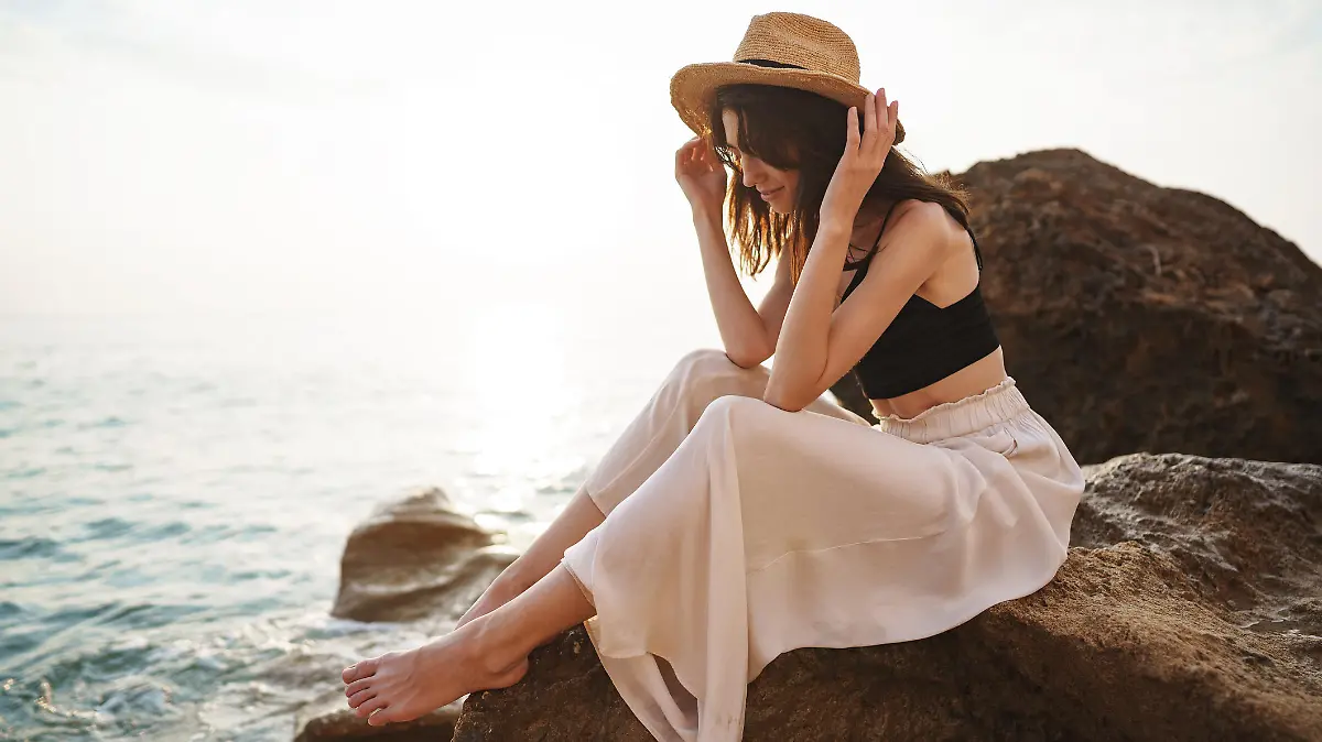 Woman traveler sitting near sea on cliff injoying view of sea and nature at summer