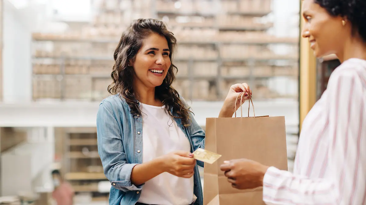 Happy female customer paying her bill with a credit card in a ceramic store. Cheerful young woman smiling happily while shopping from a local female-owned small business.