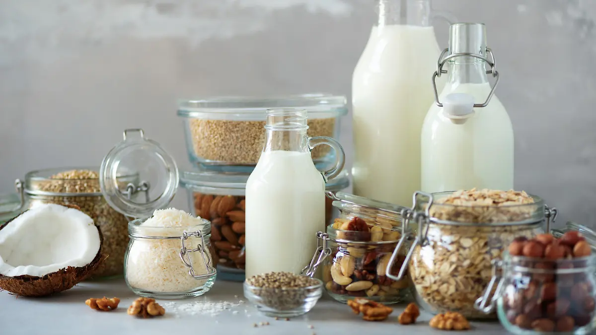 Glass bottles of vegan plant milk and almonds, nuts, coconut, hemp seed milk on grey concrete background. Banner with copy space. Dairy free milk substitute drinks and ingredients.