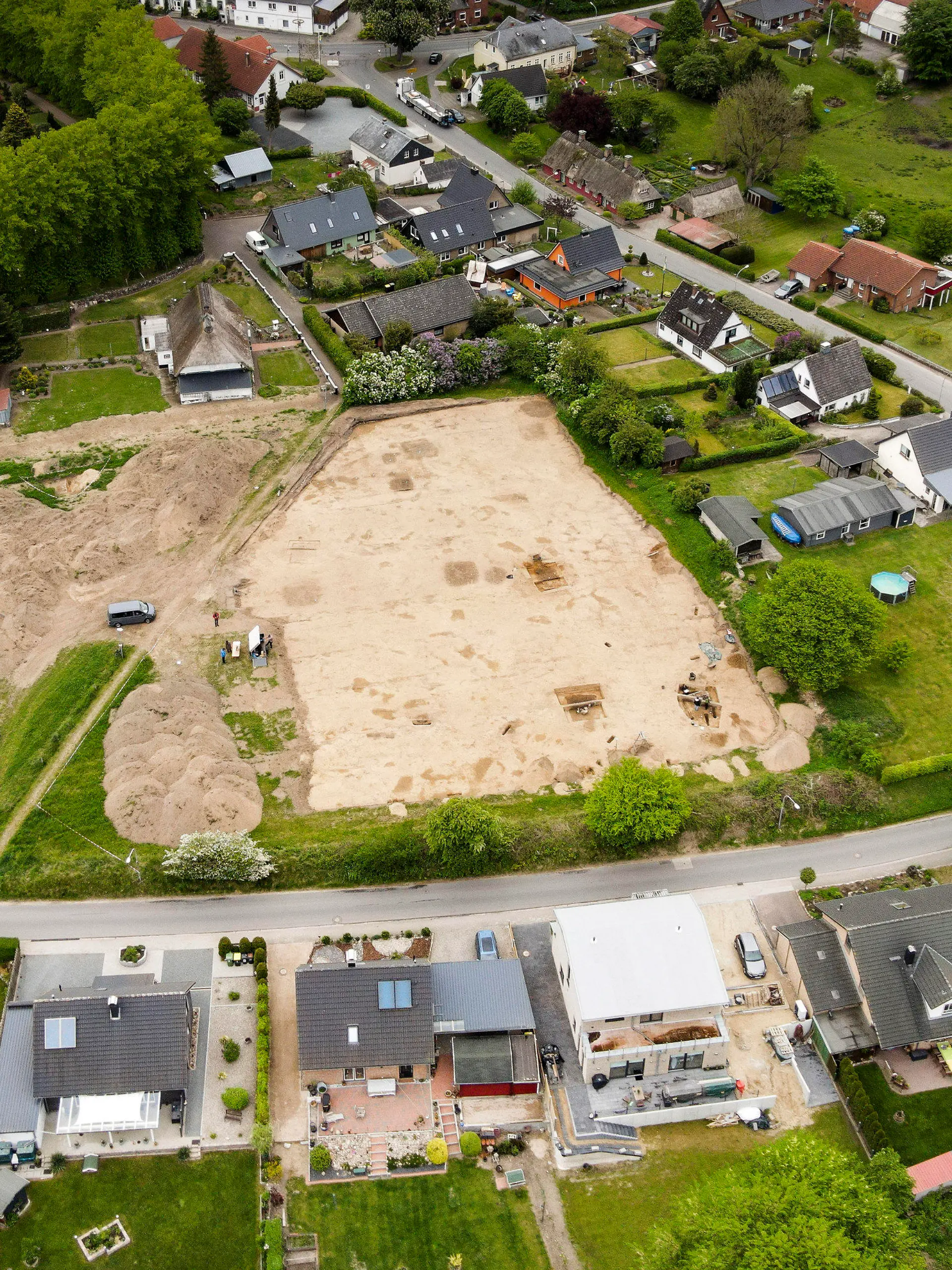 17.05.2022, Schleswig-Holstein, Süderbrarup: Ausgrabungsarbeiten werden auf einer Baustelle in einem Wohngebiet durchgeführt. Der neue wikingerzeitliche Fundplatz in Norderbrarup liegt im Ortskern in exponierter Lage nahe der über 800 Jahre alten Kirche. Er wurde im Zuge von Ausgrabungen des Archäologischen Landesamtes Schleswig-Holstein entdeckt, die im Vorfeld der Umsetzung eines hier geplanten Wohnbaugebietes durchgeführt werden. (Luftaufnahme mit Drohne) Foto: Frank Molter/dpa - ACHTUNG: Nur zur redaktionellen Verwendung im Zusammenhang mit der aktuellen Berichterstattung und nur mit vollständiger Nennung des vorstehenden Credits und Verwendung nur im vollen Format +++ dpa-Bildfunk +++