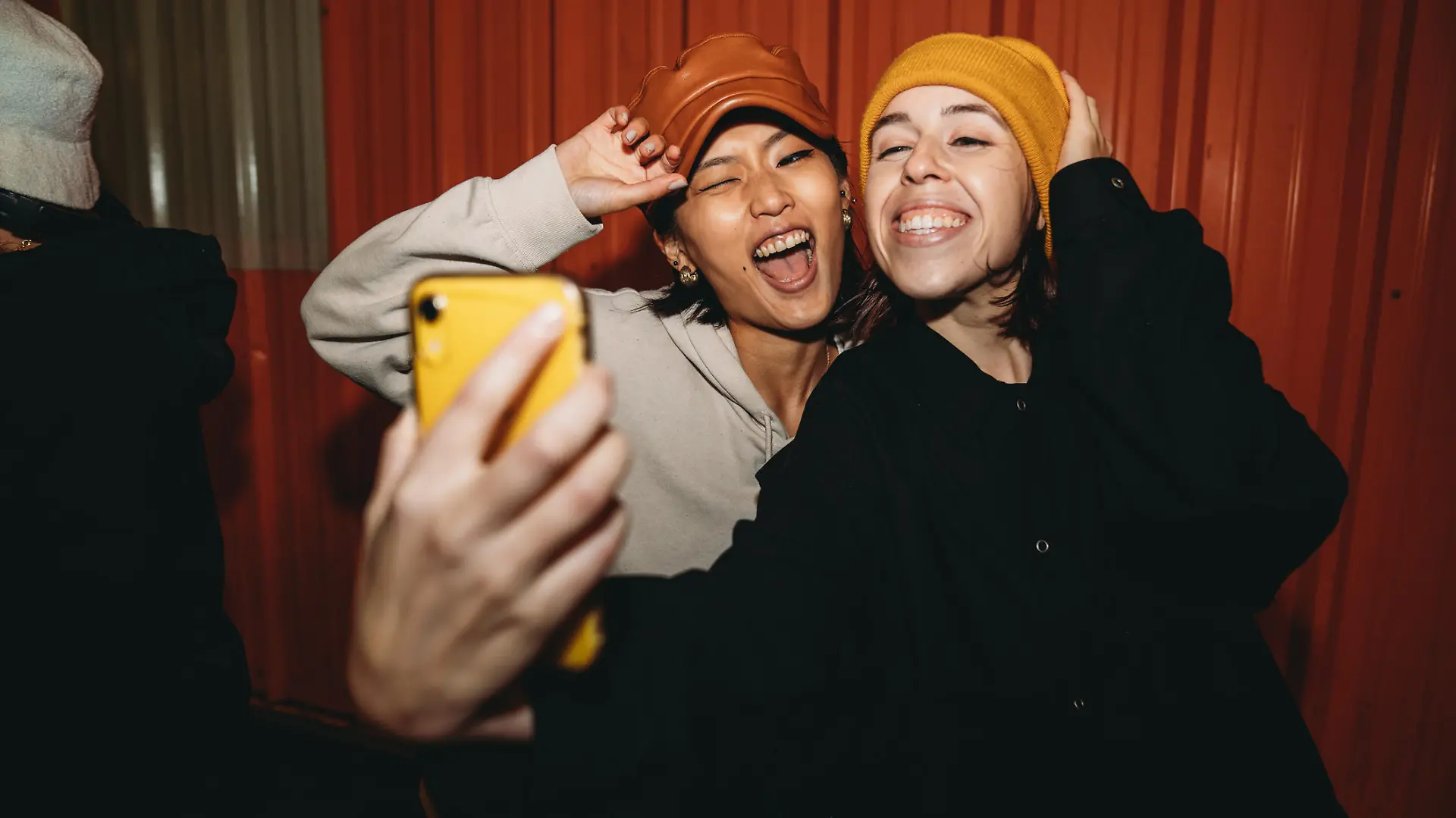 Young adult women wearing cool street style clothes are taking a selfie at night. They are wearing hats. Hip hop dancers.