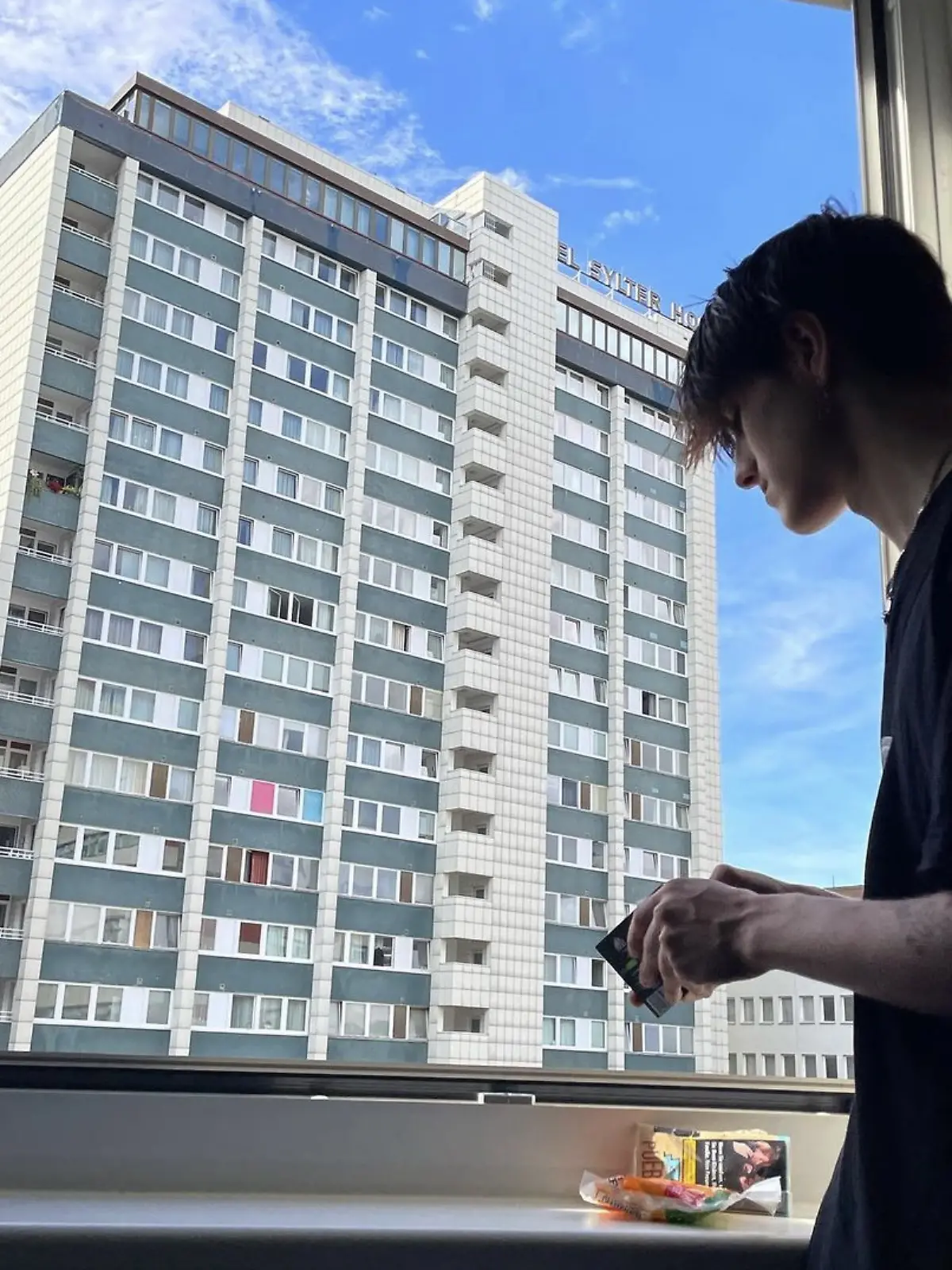 Ein junger Mann steht an einem Fenster und blickt nach draußen.