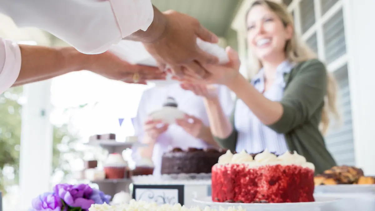 Cheerful female volunteer serves cake during a cancer awareness fundraising event. They are outdoors on the porch of a home. Delicious desserts are on the table.