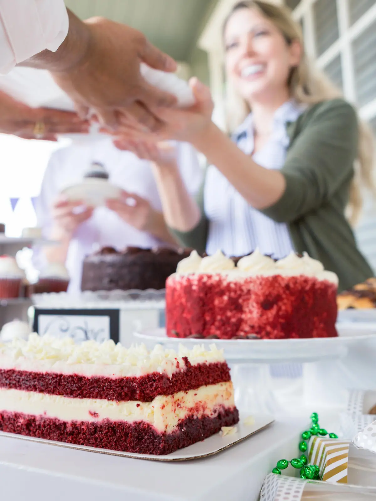 Cheerful female volunteer serves cake during a cancer awareness fundraising event. They are outdoors on the porch of a home. Delicious desserts are on the table.