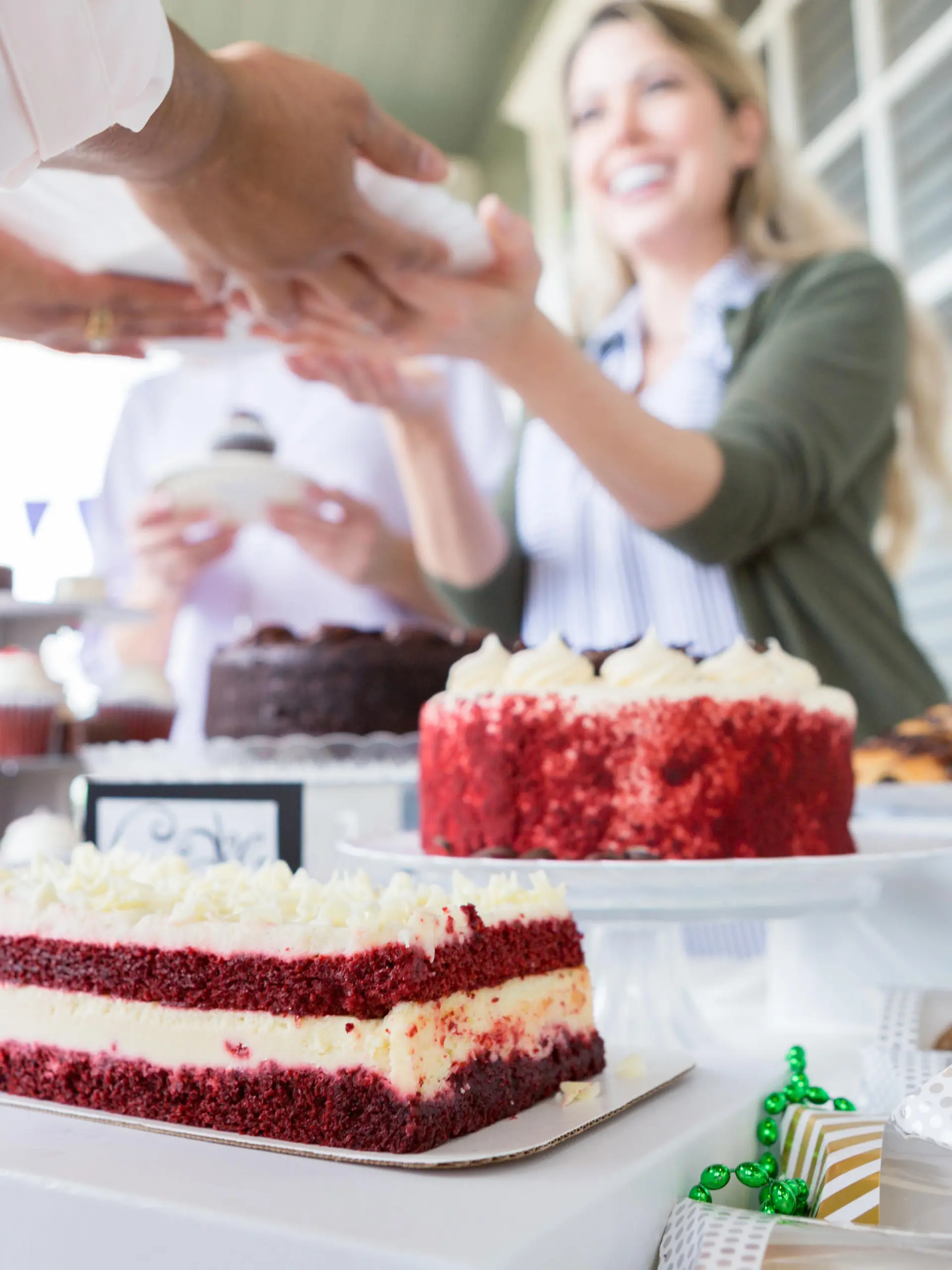 Cheerful female volunteer serves cake during a cancer awareness fundraising event. They are outdoors on the porch of a home. Delicious desserts are on the table.