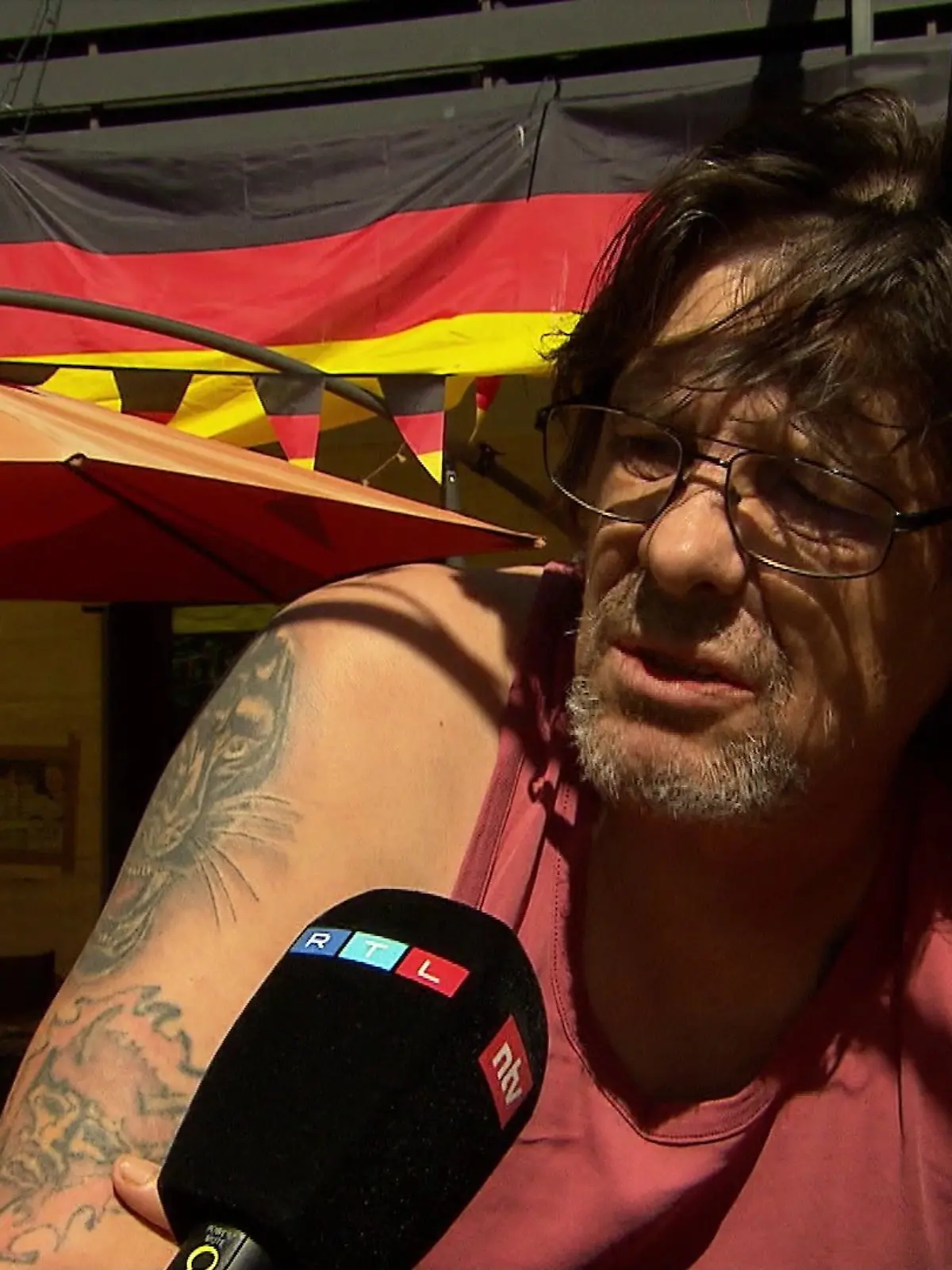 Ein Bewohner von Ahe sitzt vor einer Deutschlandflagge. Er sagt: „Wenn man mit den Leuten wenigstens vernünftig reden könnte. Die können kein Deutsch, aber meinen, die können hier die Welle reißen.“