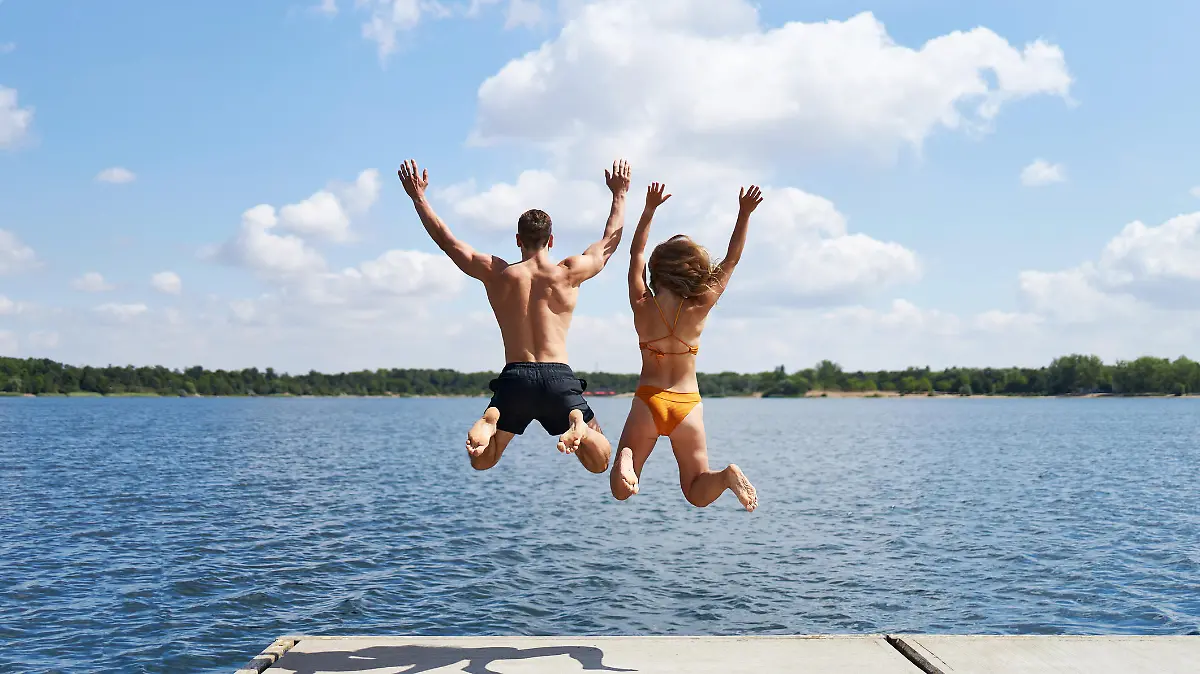 A young couple jumps from a jetty into a lake in summer in Germany