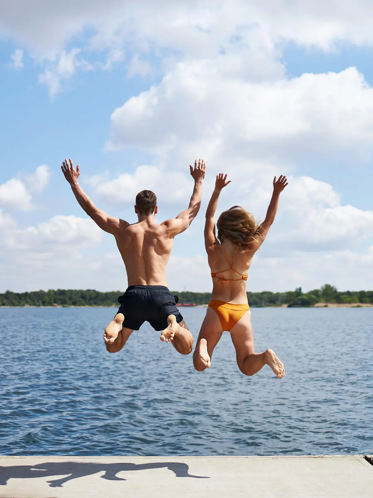 A young couple jumps from a jetty into a lake in summer in Germany