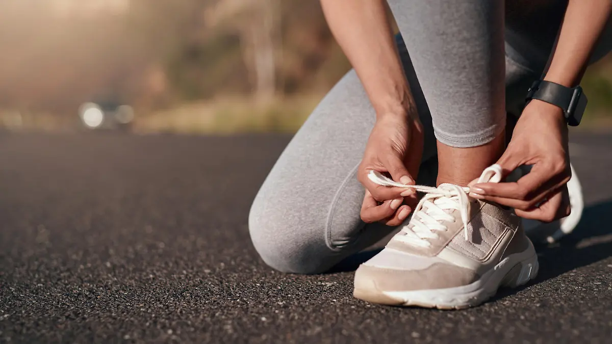 Fitness, road and woman tie her sneakers before training for a running marathon, race or competition. Sports, workout and female athlete preparing for outdoor cardio exercise for health in the street