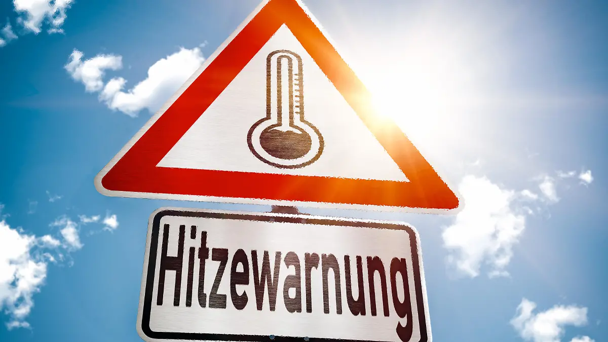 Schild vor blauem Himmel mit Sonnenschein und dem Text - Hitzewarnung, Sommer, Warnug vor Hitze, warme Temperatur FOTOMONTAGE
