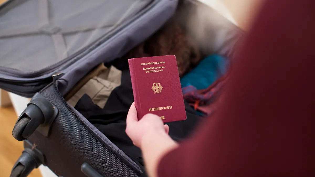 ILLUSTRATION - Eine junge Frau packt in einem Wohnzimmer in Hamburg ihren Koffer und packt den Reisepass ein (gestellte Szene). Foto: Christin Klose || Modellfreigabe vorhanden