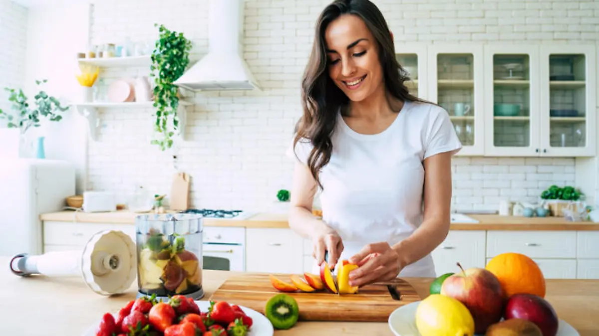 Healthy eating lifestyle concept portrait of beautiful young woman preparing drink with bananas, strawberry and kiwi at home in kitchen.