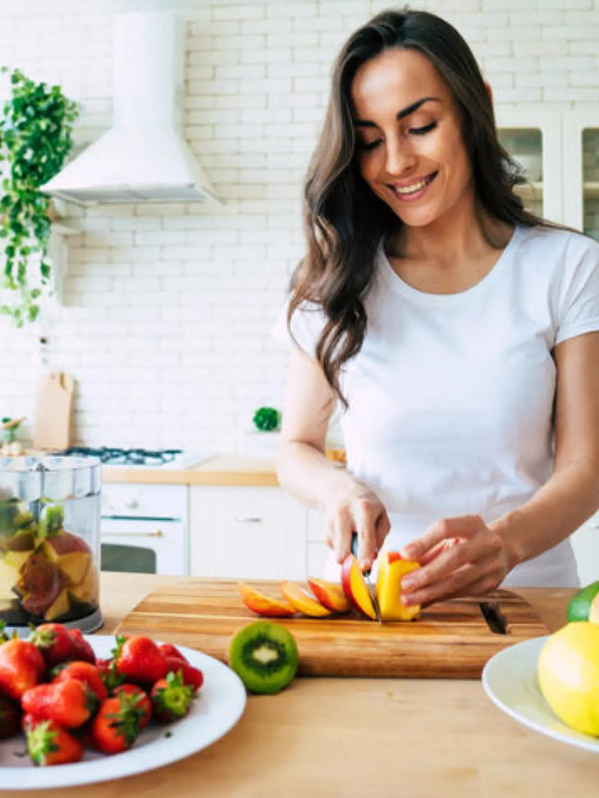 Healthy eating lifestyle concept portrait of beautiful young woman preparing drink with bananas, strawberry and kiwi at home in kitchen.