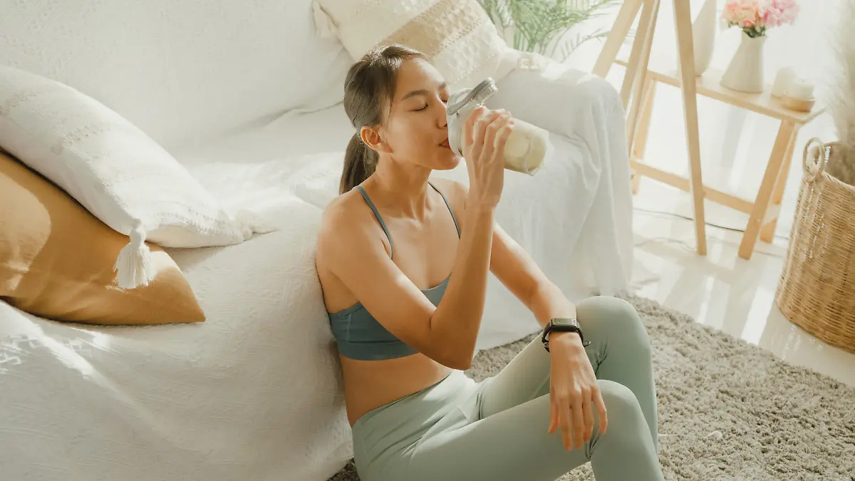 Young Asian athletic woman drinking protein shake in living room at home. Diet and healthy food concept.