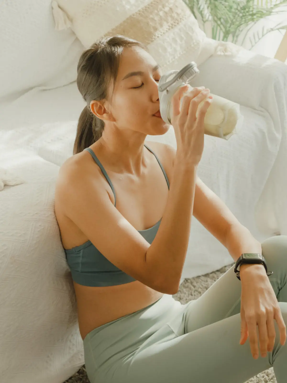 Young Asian athletic woman drinking protein shake in living room at home. Diet and healthy food concept.
