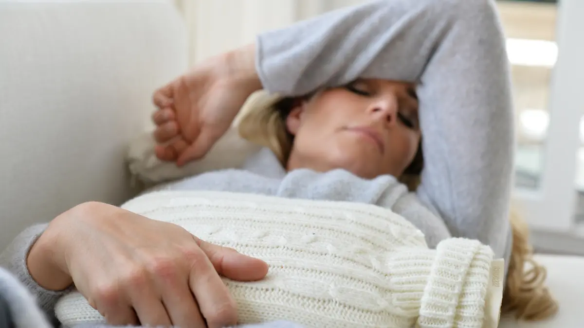 Eine Frau liegt mit einer Wärmflasche auf dem Sofa.