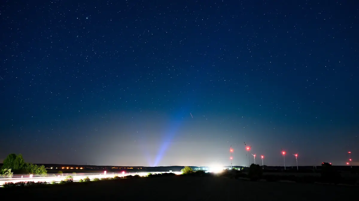 PRODUKTION - 06.05.2022, Brandenburg, Jacobsdorf: Hell erleuchtet ist die Autobahn A12, am Rand das rote Licht der Windenergieanlagen und im Hintergrund erhellt blaues Licht den Nachthimmel über der Stadt Frankfurt (Oder). Angestrahlte Kirchen und Denkmäler, Flutlicht im Stadien und grelle Straßenbeleuchtung - die Menschen machen vielerorts die Nacht zum Tag, mit verheerenden Folgen für die Tierwelt und die Artenvielfalt. (zu dpa-KORR.: "Schattenseite des Lichts: Lichtverschmutzung wird für Tiere zur Qual") Foto: Patrick Pleul/dpa +++ dpa-Bildfunk +++