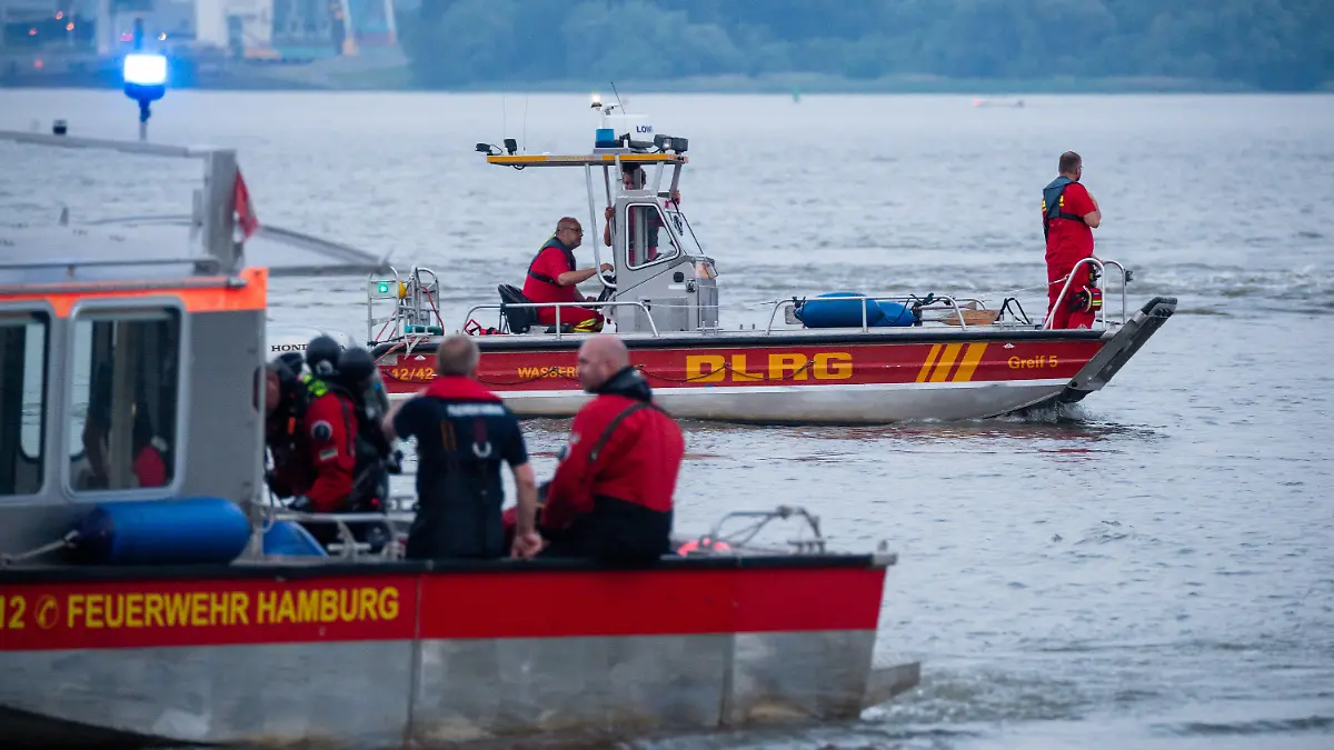 18.06.2021, Hamburg: Kleinboote von DLRG und Feuerwehr fahren bei der Suche über die Elbe. Feuerwehr und Polizei haben am Abend zweieinhalb Stunden nach einem jungen Mann gesucht, der von einem Signalturm in die Elbe gesprungen und nicht mehr aufgetaucht war. Sein Begleiter konnte laut Polizei aus dem Wasser gerettet werden. Foto: Jonas Walzberg/dpa +++ dpa-Bildfunk +++