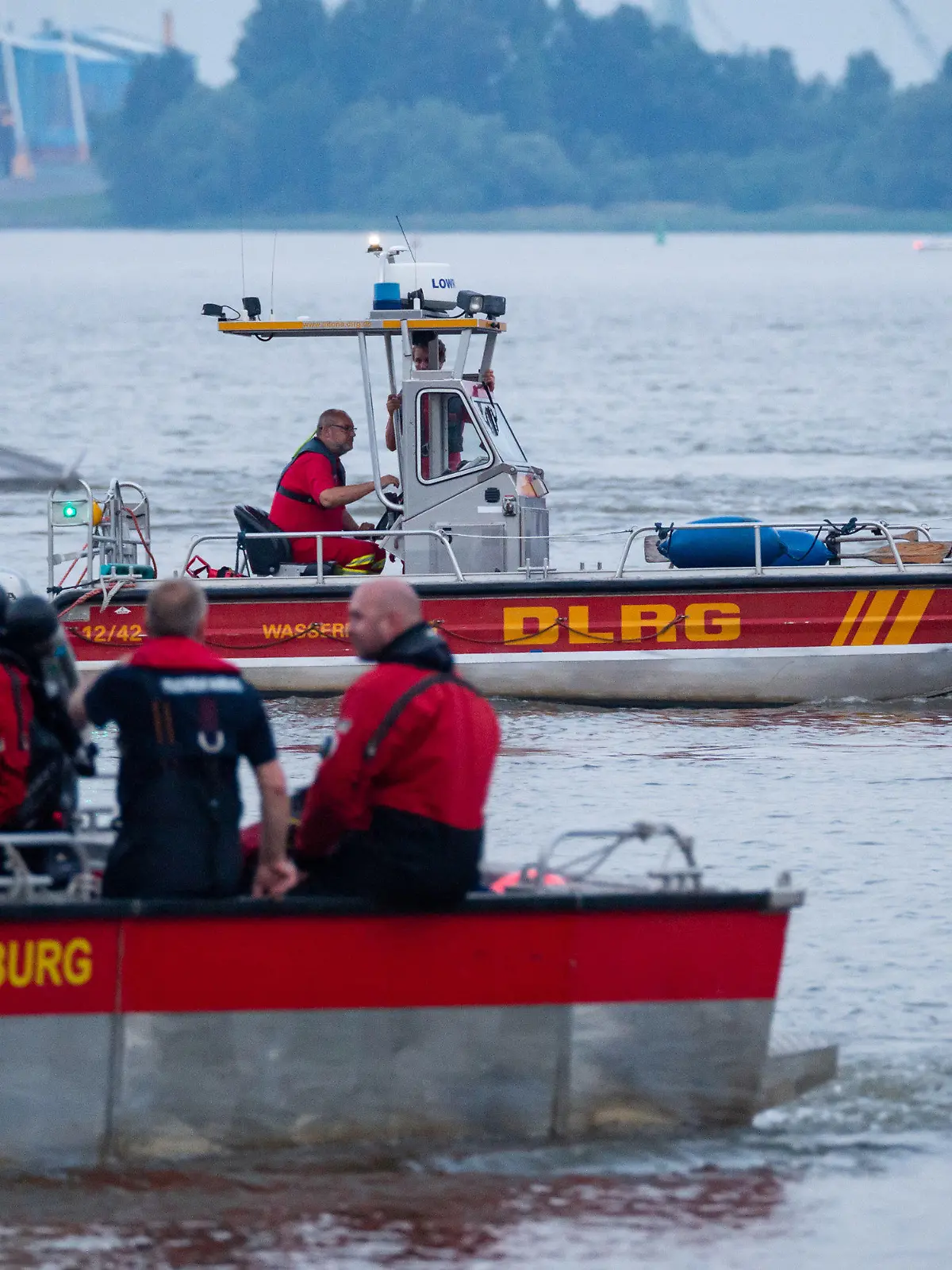 18.06.2021, Hamburg: Kleinboote von DLRG und Feuerwehr fahren bei der Suche über die Elbe. Feuerwehr und Polizei haben am Abend zweieinhalb Stunden nach einem jungen Mann gesucht, der von einem Signalturm in die Elbe gesprungen und nicht mehr aufgetaucht war. Sein Begleiter konnte laut Polizei aus dem Wasser gerettet werden. Foto: Jonas Walzberg/dpa +++ dpa-Bildfunk +++
