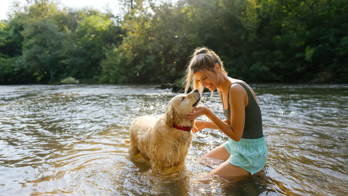 Photo of a smiling young woman and her dog bathing in the river; having a great time and enjoying the sunny afternoon outdoors.